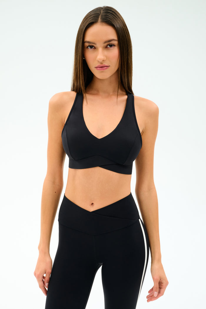A woman wears the SPLITS59 Mia Rigor Bra in black with high-waisted black leggings, standing against a plain white background—perfect for gym workouts and multi-sport performance.