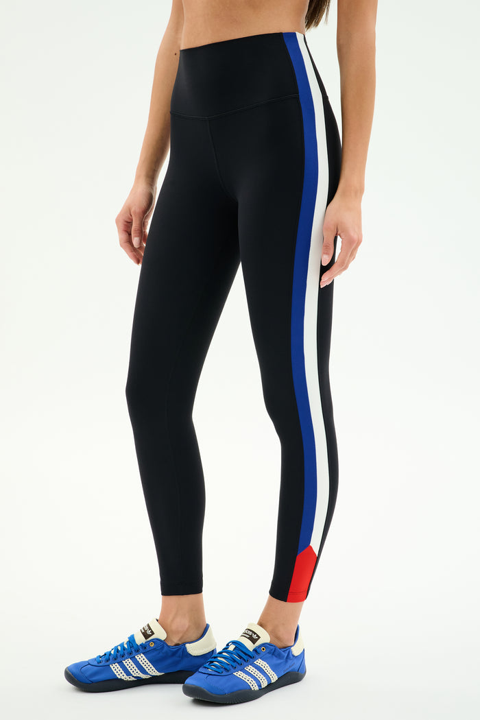 A person wearing SPLITS59 Monah High Waist Rigor Legging 7/8 in Black/Cobalt stands against a plain white background.