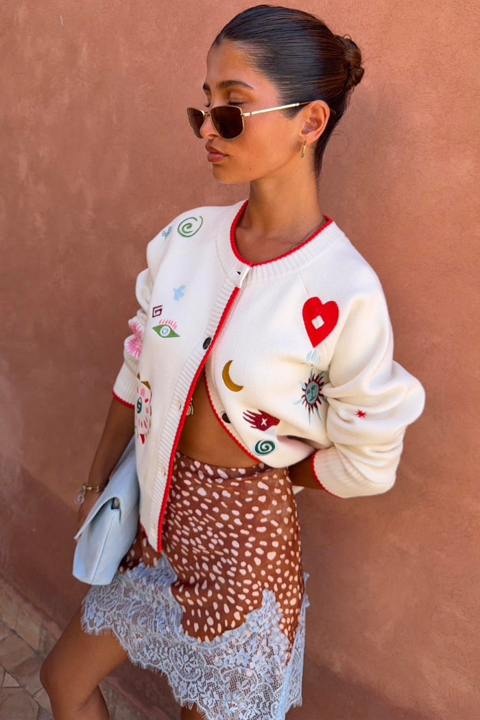Cream Morocco Charms Cheryl Cardigan featuring red trim and embroidered motifs like hearts, palms and eyes.