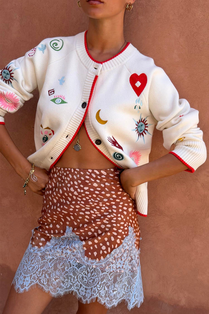 Morocco Charms Cheryl Cardigan in cream with red trim and iconic motifs, paired with a leopard print lace-hem skirt.