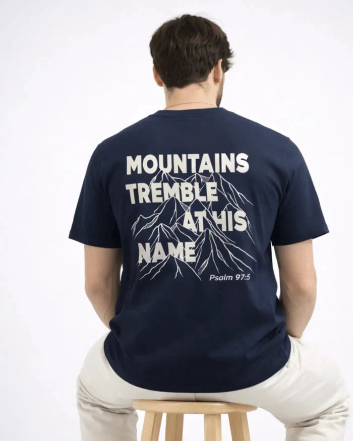 Person wearing a navy blue t-shirt with text and mountain graphic on the back, sitting on a stool.