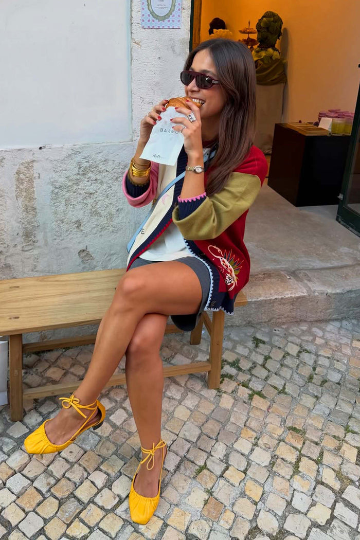 Multicoloured Mystical Martha Cardigan with embroidered motifs and blanket stitching, styled on a woman sitting outdoors.