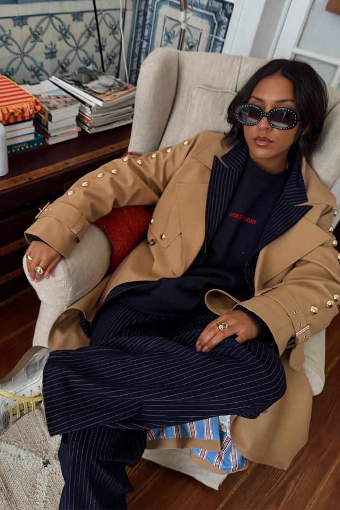 Navy Book The Flight Jumper with red text, layered with a tan studded trench and pinstripe trousers.