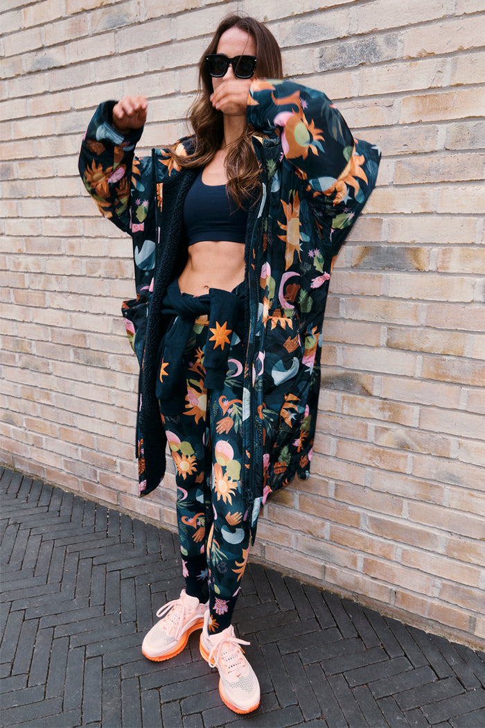 Waterproof Navy Charm Coat with a colourful sun and moon motif print and fleece lining, styled against a brick wall.
