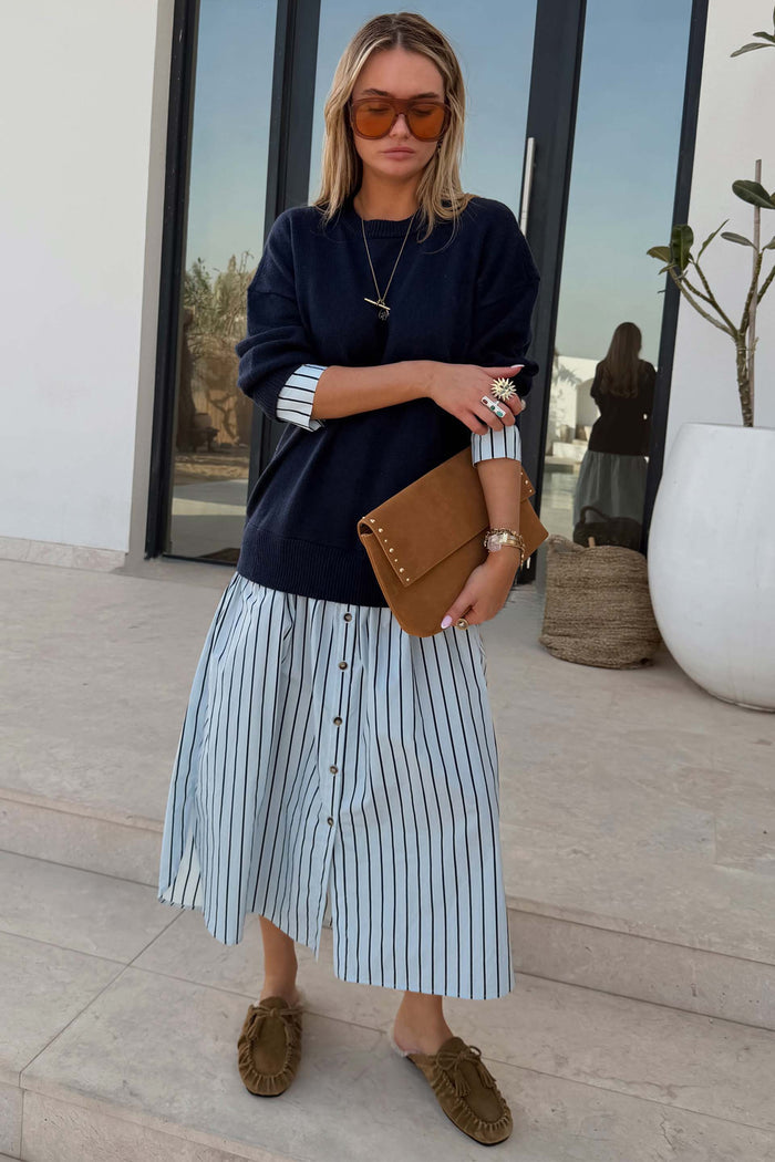 Navy Knit Jumper Dress featuring a blue stripe cotton skirt, styled with a brown clutch and oversized sunglasses.