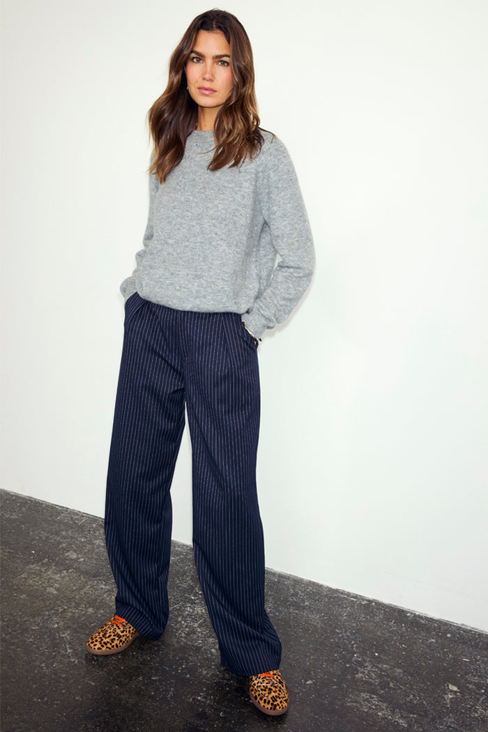 Navy Pinstripe Arden Trousers in a wide-leg fit, styled with a grey knitted jumper and leopard print shoes.
