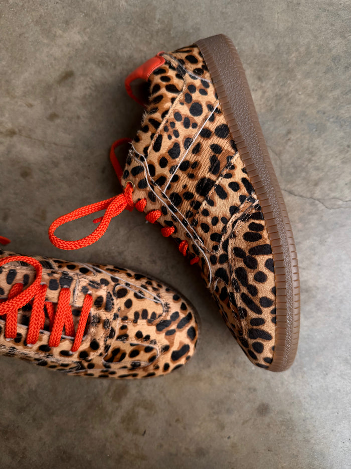 Leopard Pony Trainer featuring textured leopard print, vibrant orange laces, and a gum sole on a concrete surface.