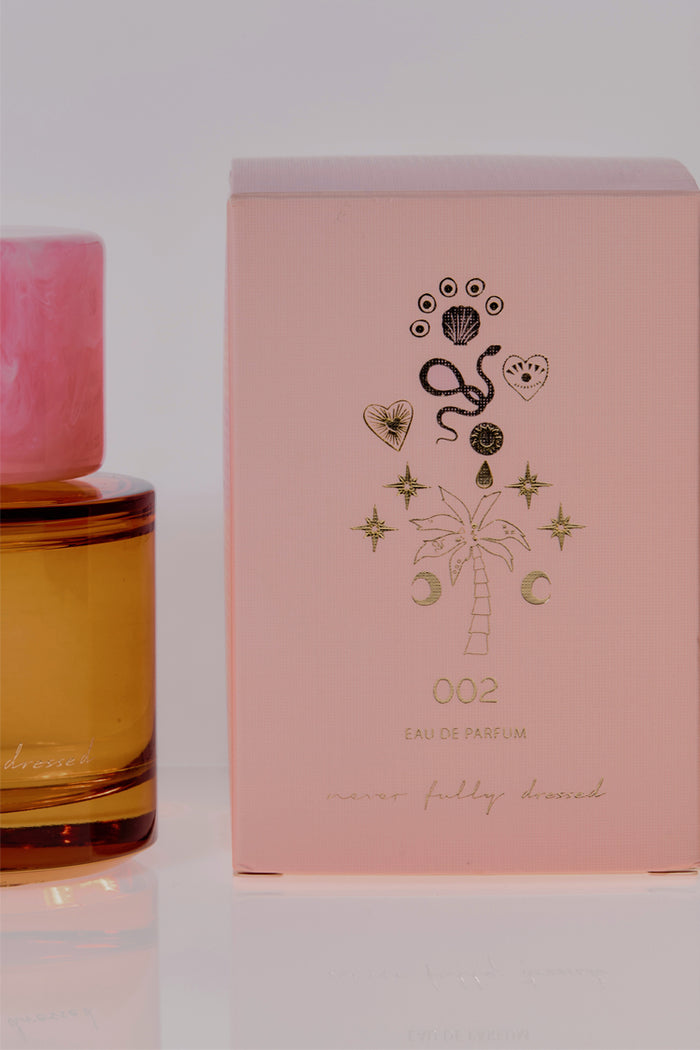 NFD Eau De Parfum 002 amber bottle with a pink marble cap next to a pale pink box with gold foil illustrations.