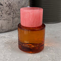 NFD Eau De Parfum 002 bottle in amber glass with a pink marbled cap, set on a textured grey stone surface.