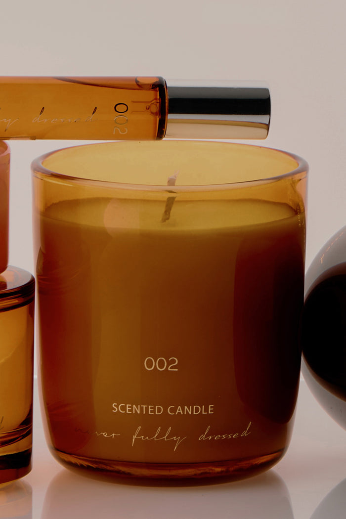 NFD Scent 002 Candle in an amber glass jar with gold lettering, paired with the matching perfume bottle.