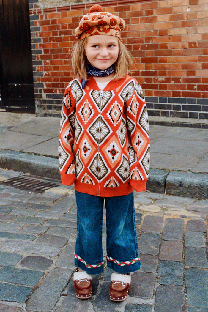 NFD Kids Diamond Bomber in a rust orange knit with a bold diamond pattern, worn by a child on a London street.