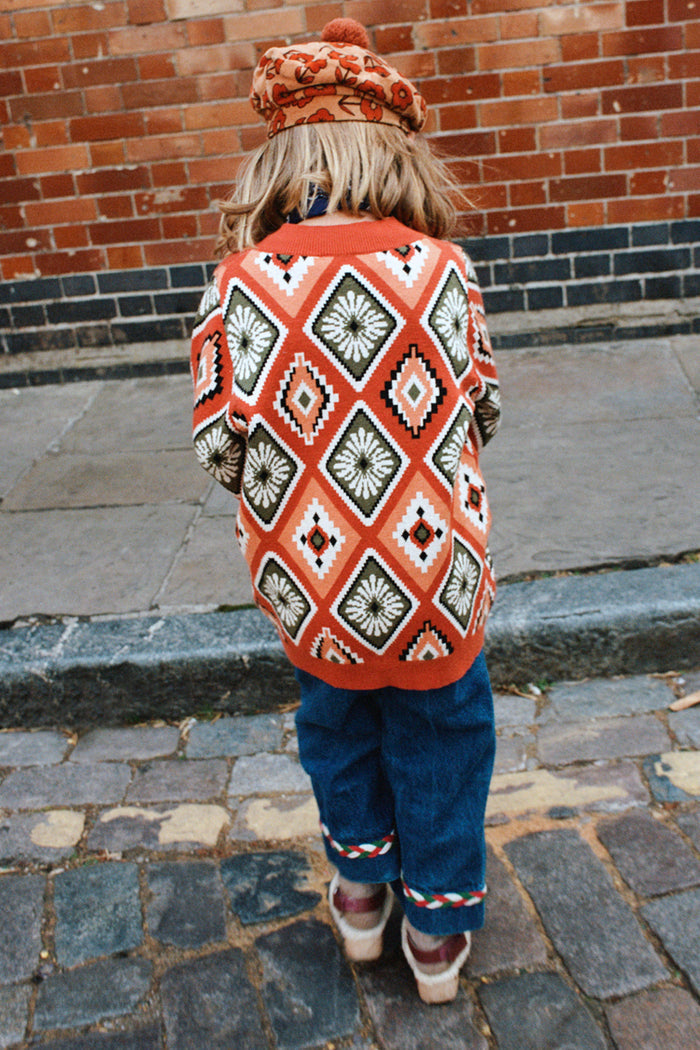 NFD Kids Diamond Bomber in rust orange with olive and red diamond patterns, worn by a child on a cobbled street.