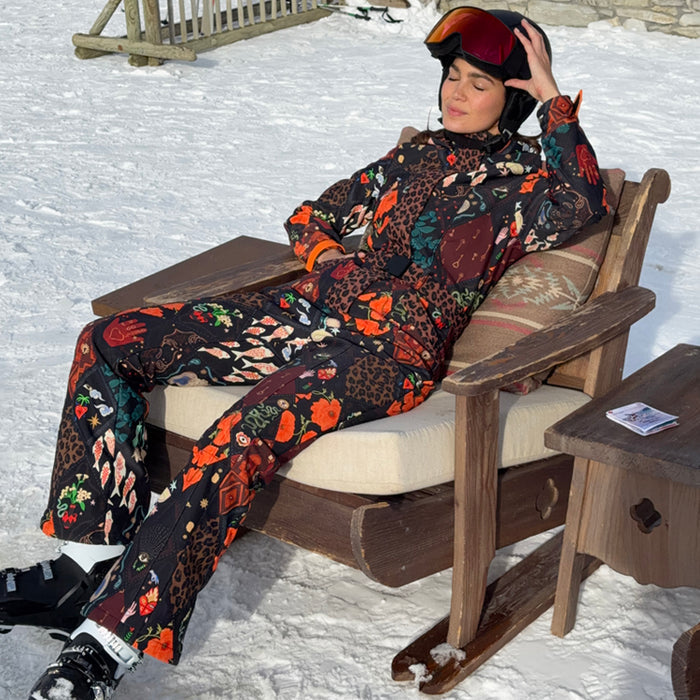 Night Garden Ski Suit featuring leopard and poppy prints, worn by a woman lounging at a snowy ski resort.
