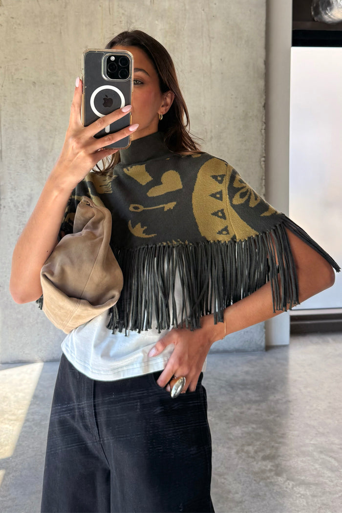 Olive Amara Knit Cape with a turtle neck, tassel fringe and hand-painted motifs, shown on a model.