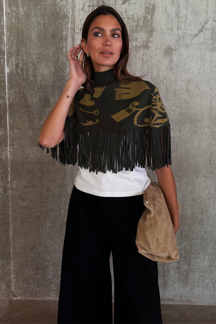 Olive Amara Knit Cape featuring a turtle neck and long fringe trim with gold floral and heart motifs.