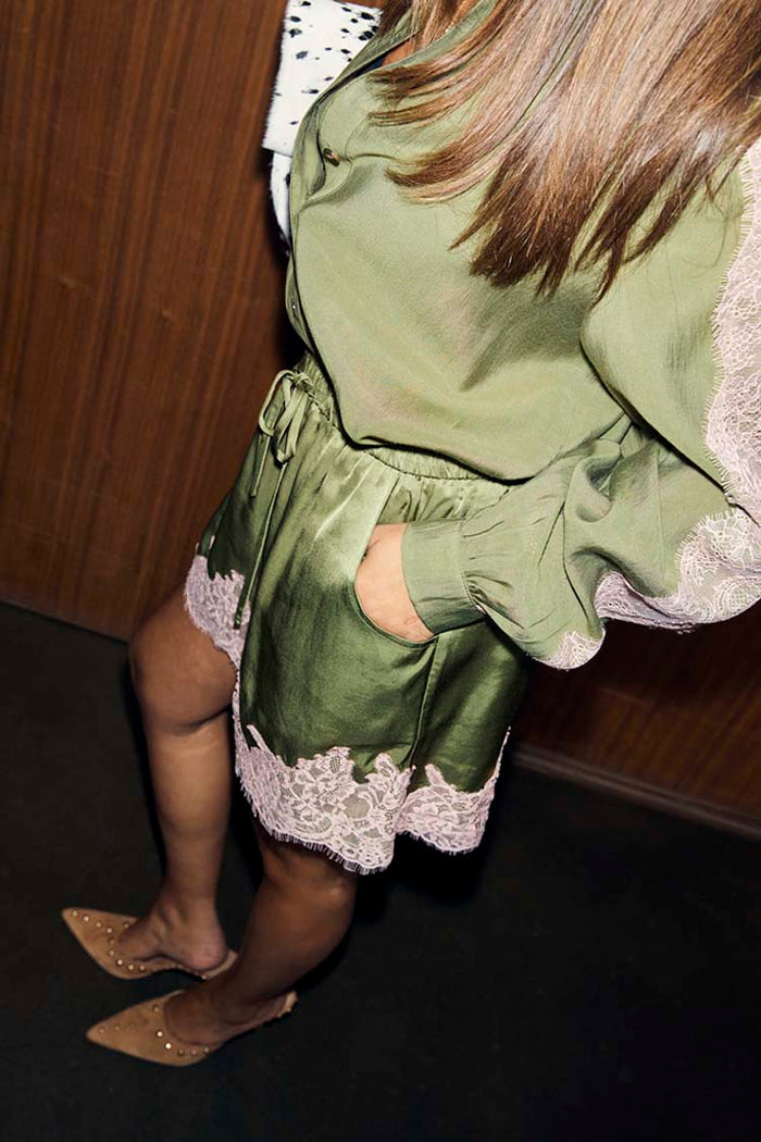 Olive green satin shorts with a pink lace hem and drawstring waist, styled with a matching olive shirt.