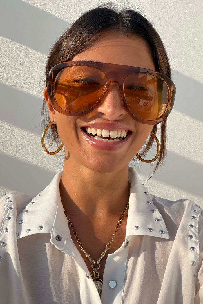 Orange Acetate Visor Sunglasses on a smiling model with 70s-inspired tinted lenses and gold hoop earrings.