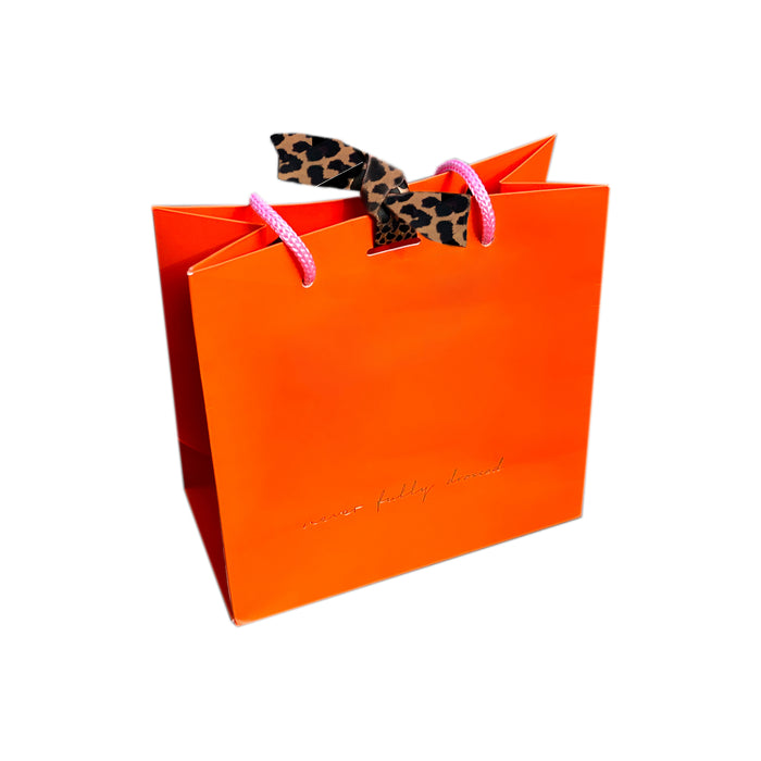 Vibrant orange NFD gift bag featuring pink rope handles, gold foil branding, and a signature leopard print tie.