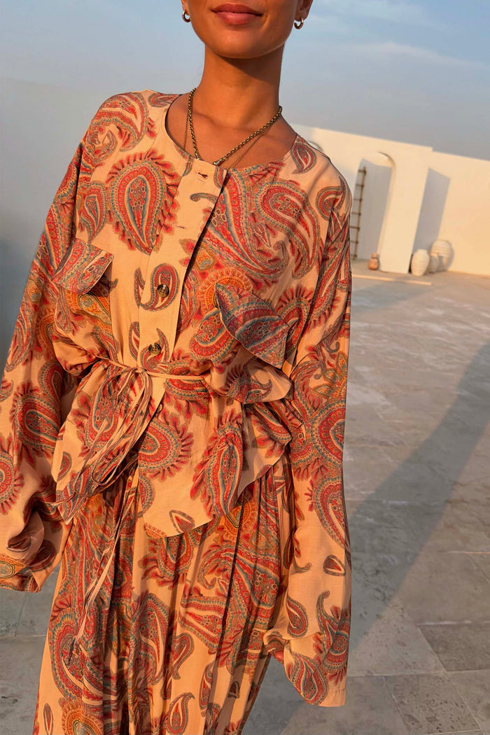 Peach Paisley Anna Top with a button-through front and tie waist, worn in a sunny outdoor terrace setting.