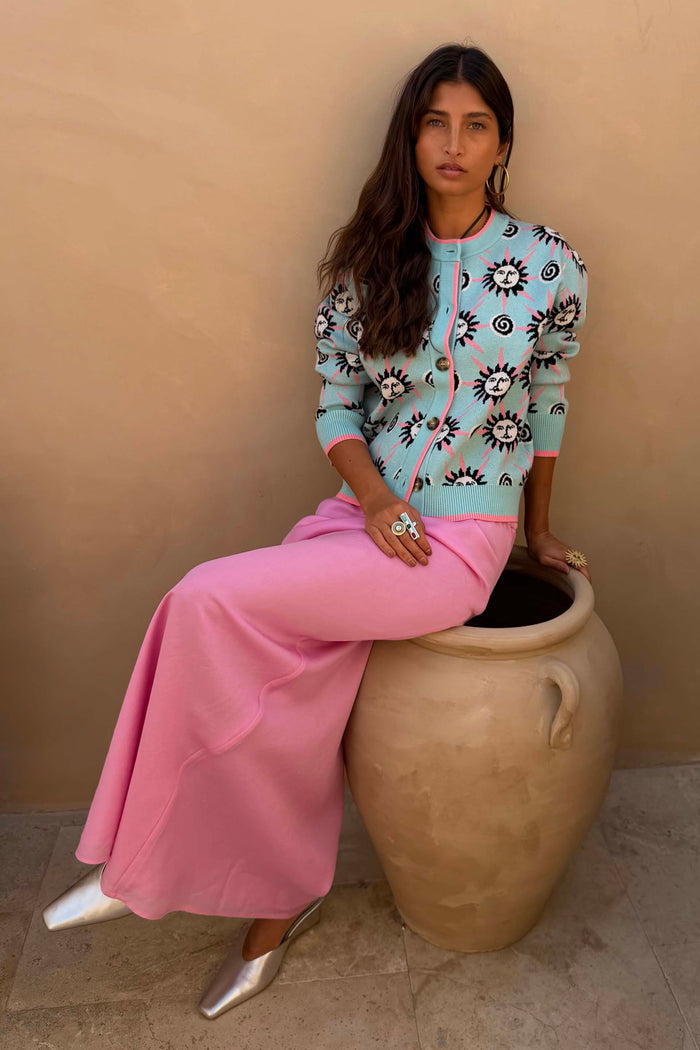 High-waisted Pink Daphne Skirt in a soft pink tone, paired with a sun-motif cardigan and silver pointed mules.