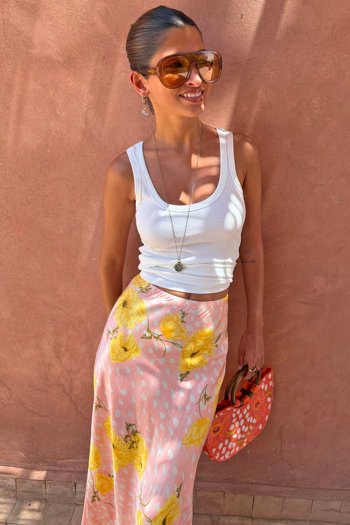 Pink Fawn Poppy Midi Maeva Skirt with yellow floral motifs, styled with a white ribbed tank top and sunglasses.