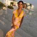 Pink Fawn Poppy Olivia Dress featuring yellow lace trim and a vibrant poppy print, worn by a pool at sunset.