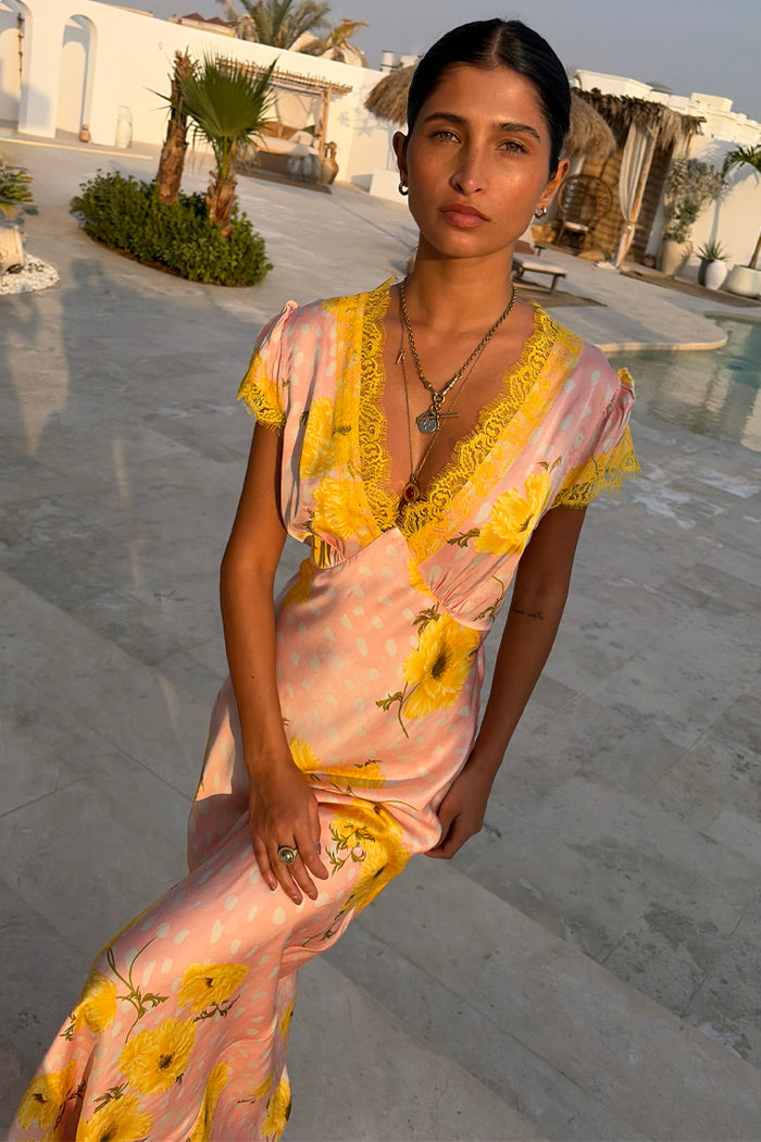 Pink Fawn Poppy Olivia Dress with yellow lace trim and a V-neckline in a vacation setting.