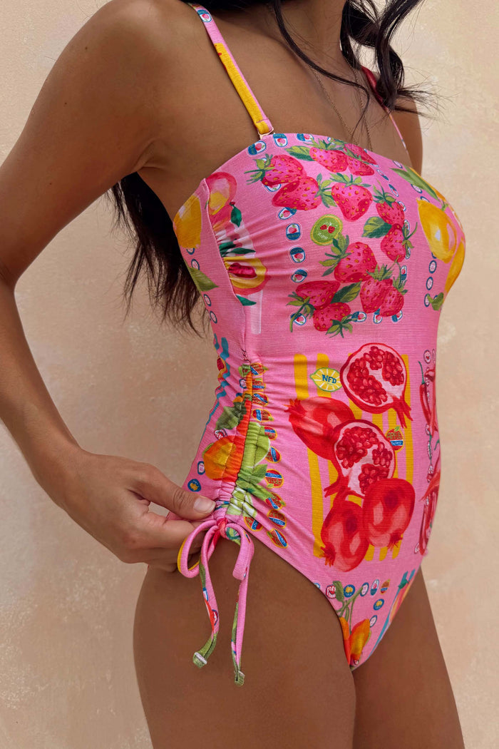 Pink bandeau swimsuit featuring a Mediterranean fruit stamp print, adjustable ruched side seams and tie details.