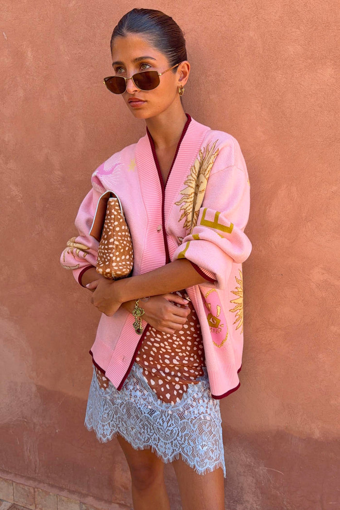 Pink Mystical Cardigan with jacquard sun and moon motifs and burgundy trims, styled with a lace-trimmed dress.
