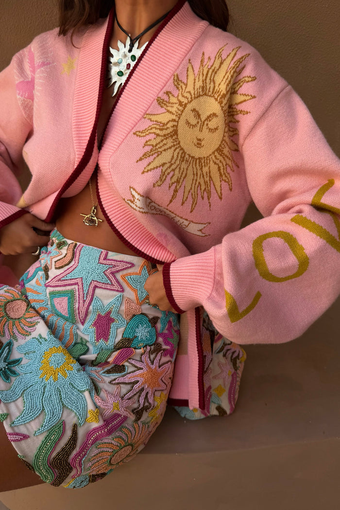 Pink Mystical Cardigan with gold jacquard sun motifs and burgundy trims, paired with a colourful beaded star skirt.