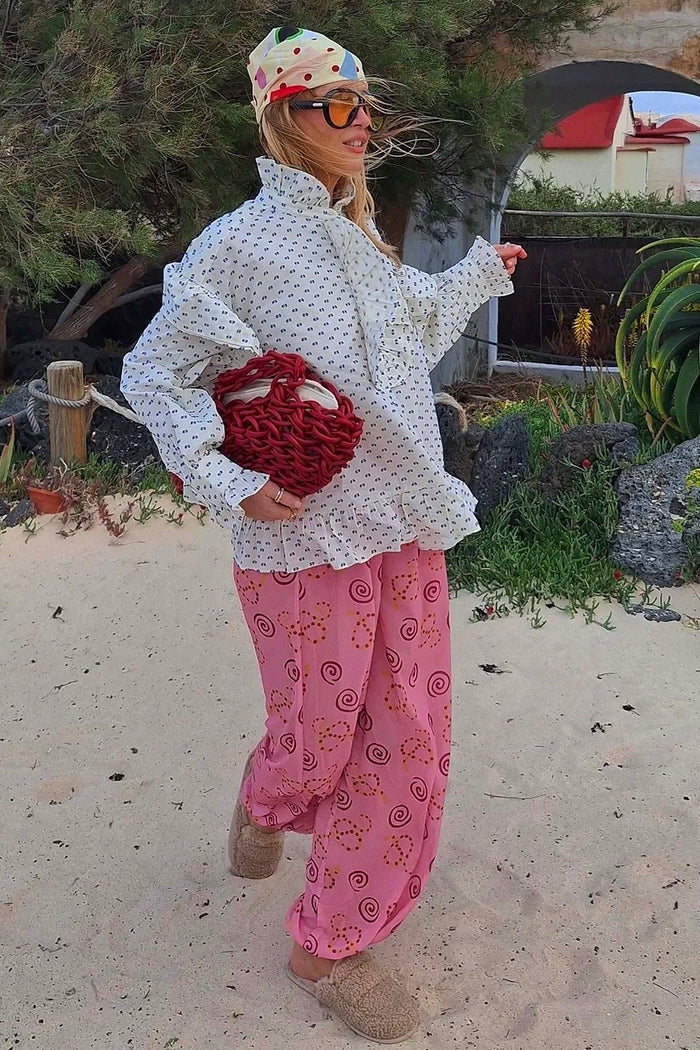 Dusky Pink Snake Balloon Trouser with snake and swirl motifs, styled with a white ruffled blouse on a sandy beach.