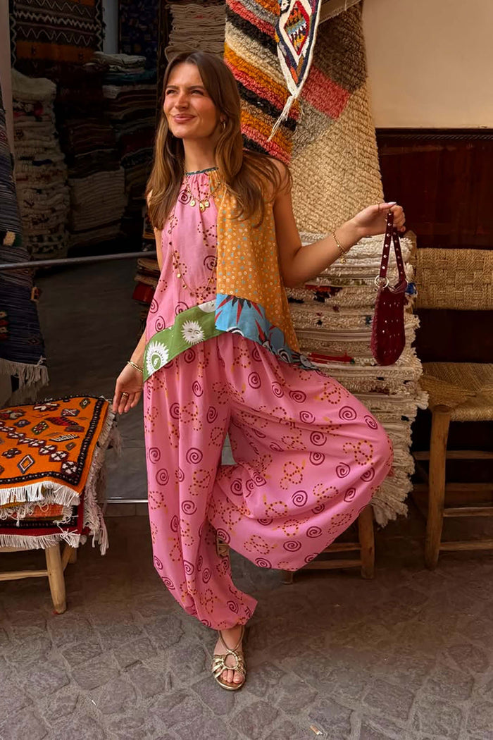 Pink Snake Balloon Trousers with snake and swirl motifs, styled with a patchwork top in a rustic textile market.