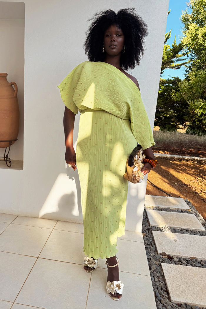 Pistachio Tilly Dress in green plisse with gold flecks, styled off-the-shoulder for an elegant wedding guest look.