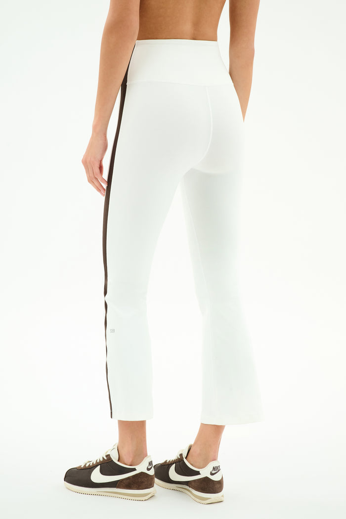 A person is shown from the back wearing SPLITS59 Raquel High Waist Supplex Crop in White/Dark Chocolate, featuring a high-waisted fit and dark chocolate side stripe, paired with black Nike sneakers against a plain background.