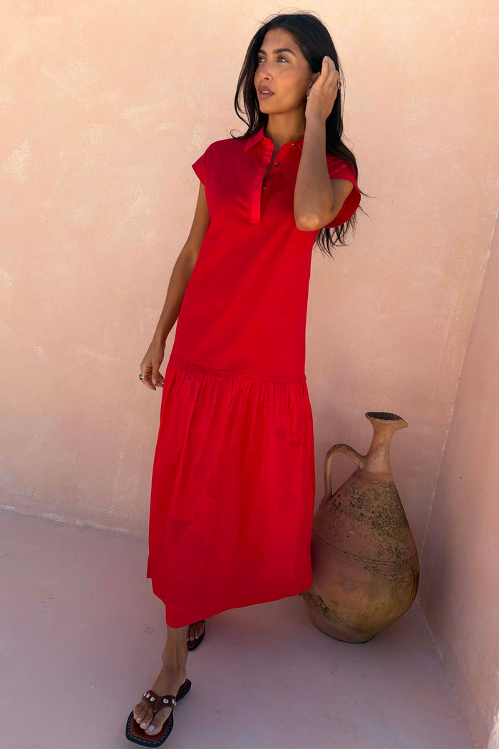 Red Darcy cotton midi dress featuring a dropped waist and collared neckline, standing beside a large ceramic vase.