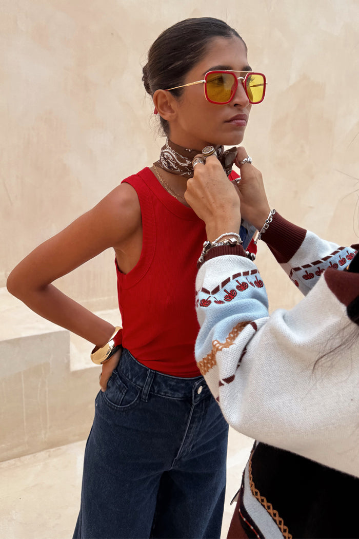 Red ribbed tank top styled with dark denim jeans, yellow sunglasses and a patterned neck scarf.