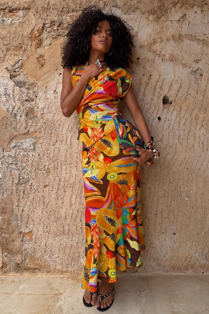 Rio A-Symmetric Skirt in a tropical fruit print with an angled hem, styled as a co-ord against a textured wall.