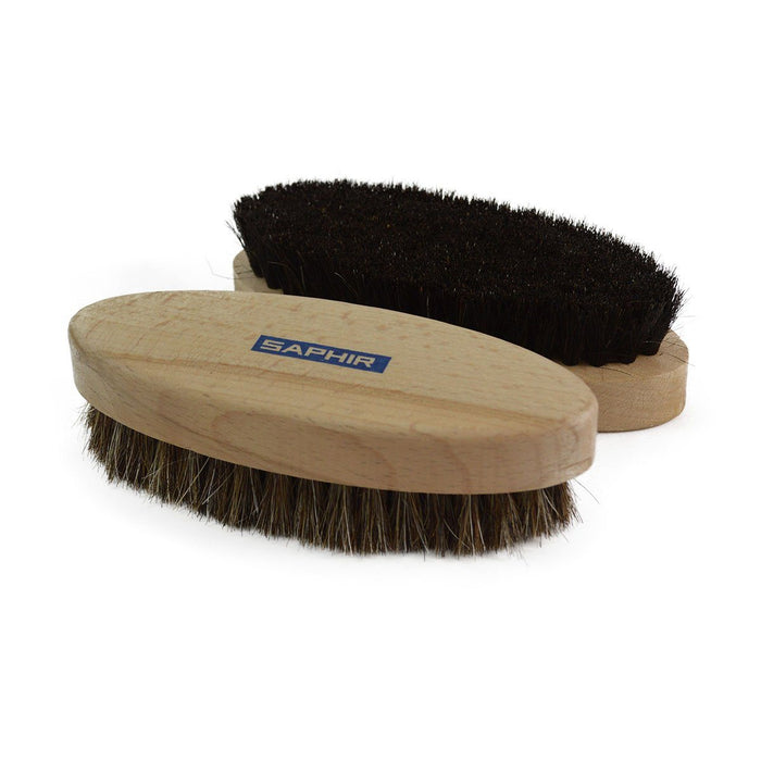 Two oval shoe shine brushes with horsehair bristles, one with black bristles and one with natural brown bristles, both with wooden handles, on a white background.