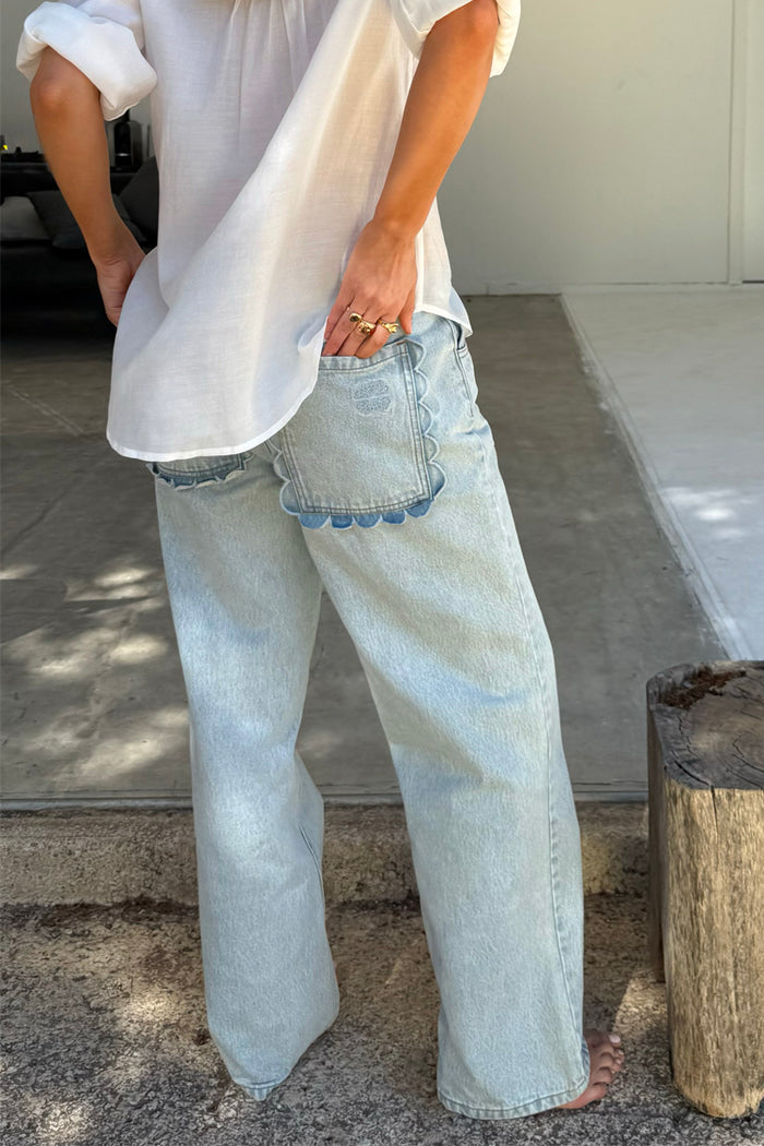 Light blue straight leg denim jeans with scalloped back pockets, styled with a white shirt.