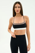 A woman stands against a plain background wearing the SPLITS59 Scottie Airweight Bra in Black/Lentil with white trim and matching high-waisted leggings, both crafted from soft nylon and spandex for a comfortable, flexible fit.