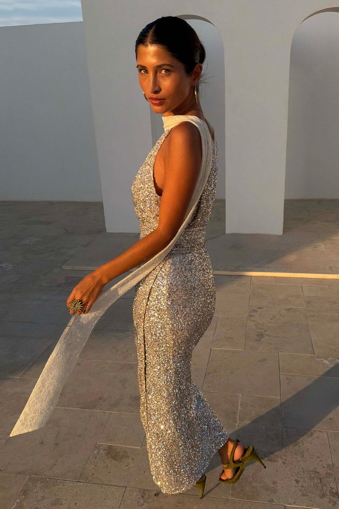 Silver Sequin Maxi Wrap Jaspre Skirt with a waist tie, styled in an outdoor architectural setting.
