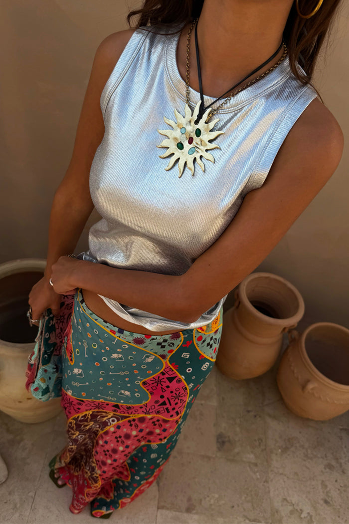 Metallic silver ribbed tank top styled with a colourful patterned skirt and statement sun necklace.