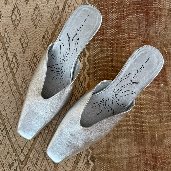 Silver Wedge Mule in metallic real leather with a pointed toe and signature printed insole on a textured rug.