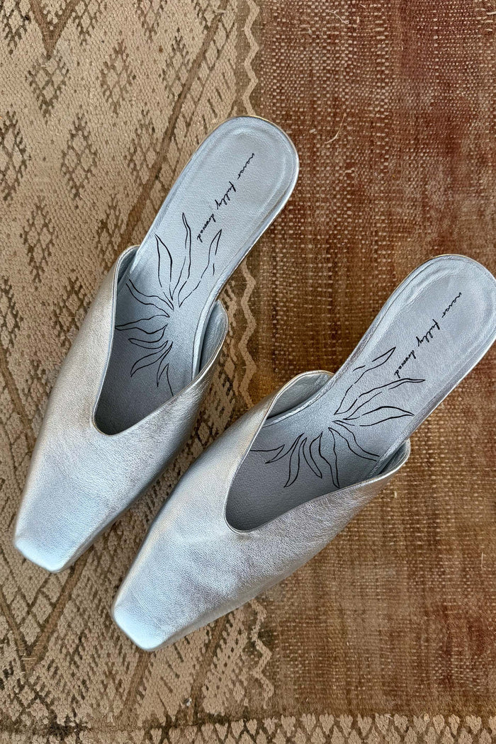 Silver Wedge Mules in metallic real leather with a pointed toe and illustrated insole on a textured rug.
