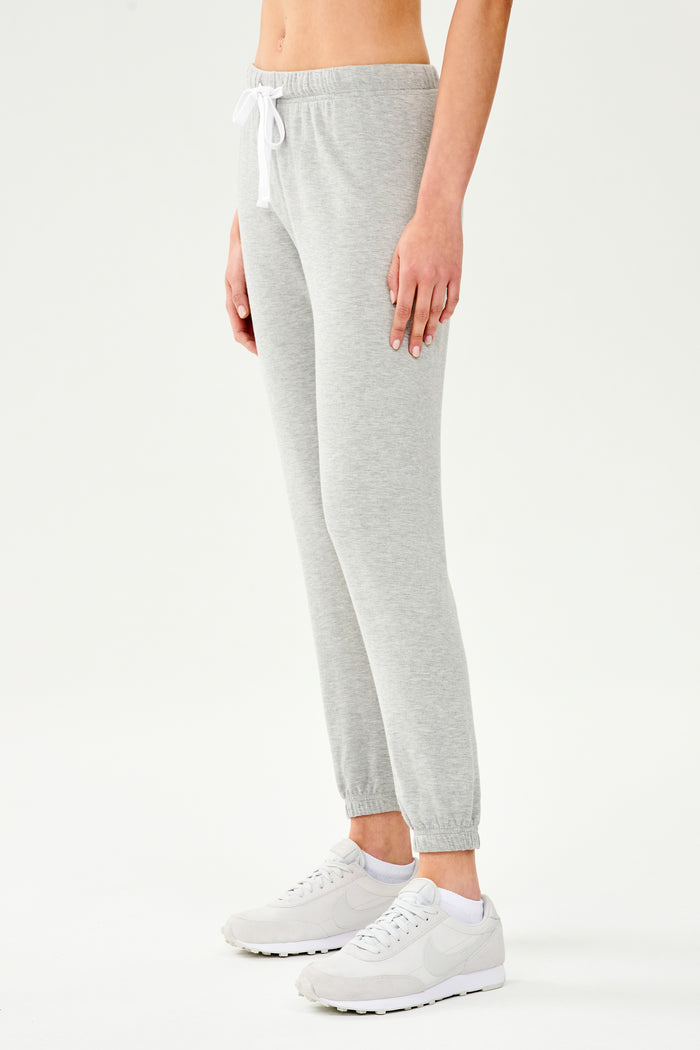Front side view of woman wearing light grey jogger with white drawstring and white cropped tank top paired with creme shoes