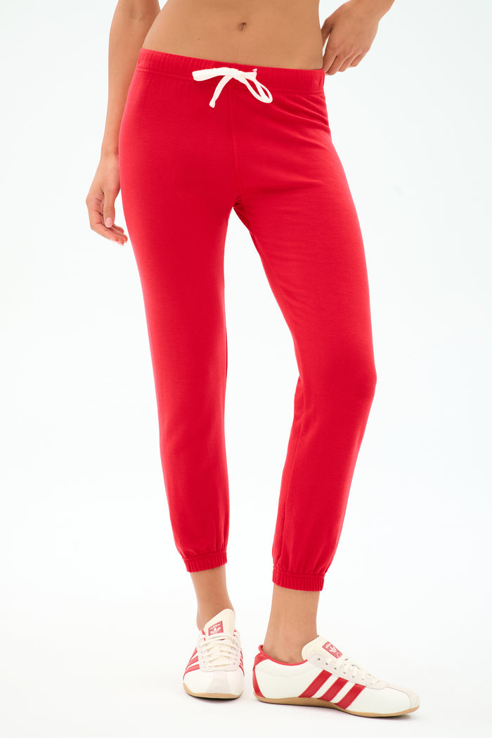 Wearing the SPLITS59 Sonja Fleece Sweatpant in Pirate Red, styled with a white drawstring and paired with white sneakers featuring red stripes, this look exudes relaxed Los Angeles vibes against a simple backdrop.