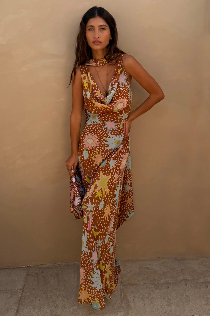 Star Fawn Sophie Dress in brown with sun and star motifs, featuring a draped neck, scarf, and clutch bag.