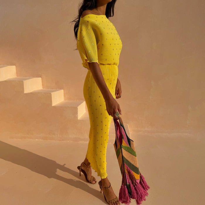 Yellow plissé Sunshine Tilly Dress with gold flecks, styled off-the-shoulder with a colourful tassel bag.