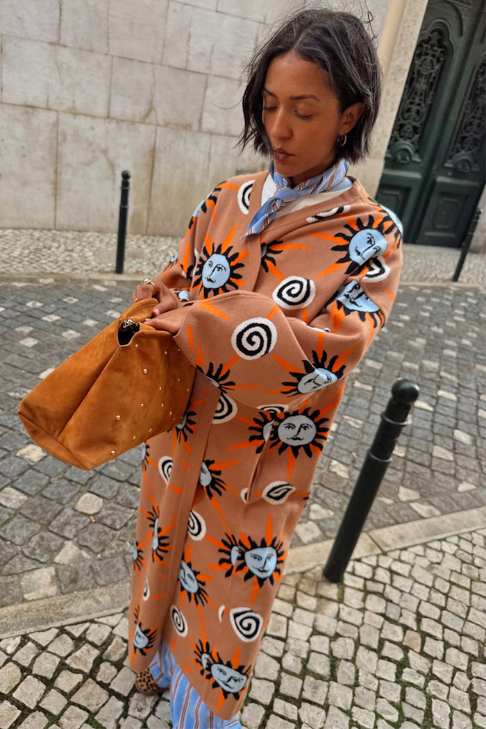 Tan Sun Cardigan with hand-painted sun motifs and dropped shoulders, styled on a cobblestone street.