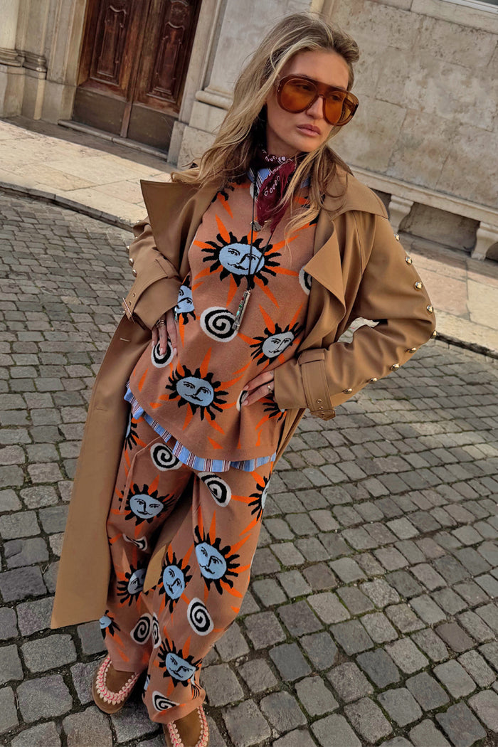 Tan Sun Copenhagen Jumper with sun and swirl motifs, styled with matching trousers and a long camel trench coat.